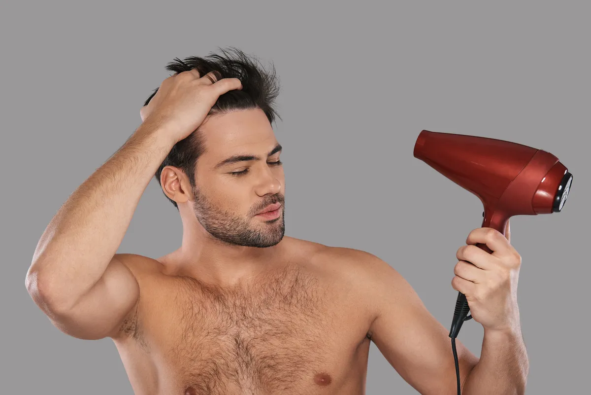 Mężczyzna wysusza włosy suszarką