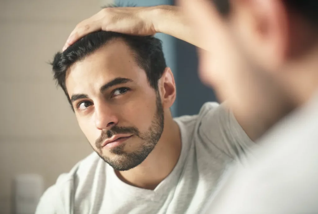 Mężczyzna patrzy w lustro na swoje włosy